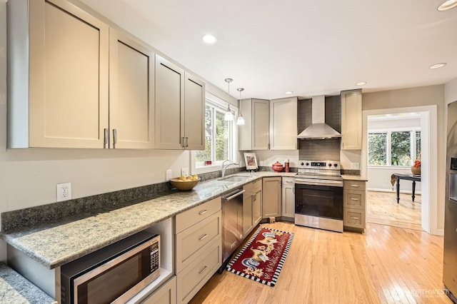 kitchen with wall chimney range hood, stainless steel appliances, a healthy amount of sunlight, and a sink