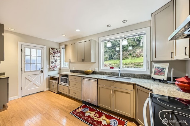 kitchen with wall chimney exhaust hood, a sink, light wood-style flooring, hanging light fixtures, and stainless steel appliances