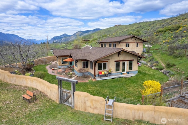 view of front of house featuring fence private yard, a gate, a front lawn, a deck with mountain view, and stucco siding