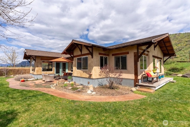 back of property with stucco siding, a yard, and a wooden deck