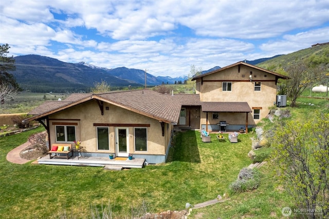 rear view of house with a lawn, central AC unit, a deck with mountain view, and stucco siding