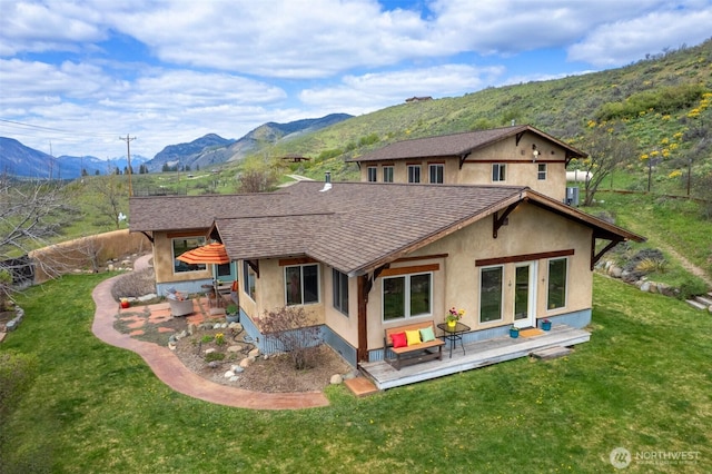 rear view of property with roof with shingles, stucco siding, a yard, and an outdoor hangout area