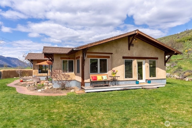 rear view of house featuring stucco siding, a deck with mountain view, and a yard