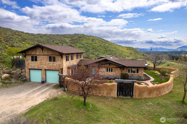 view of front facade featuring a garage, a mountain view, stucco siding, and dirt driveway
