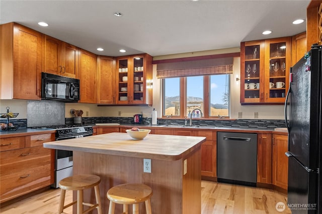 kitchen featuring butcher block countertops, a kitchen bar, light wood-type flooring, a sink, and black appliances