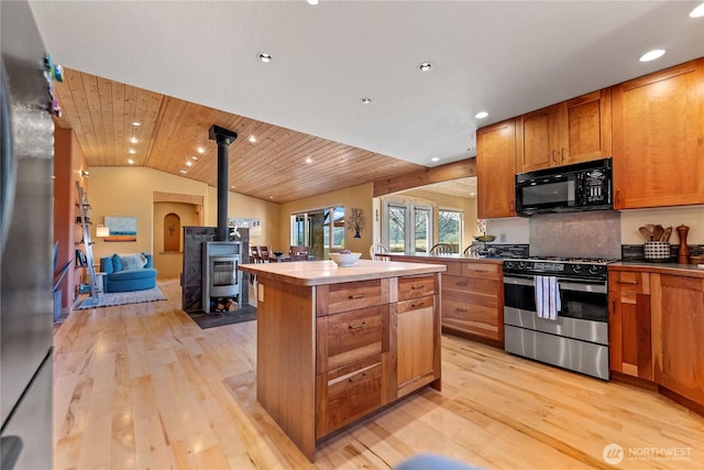 kitchen featuring a wood stove, lofted ceiling, a center island, light wood-style flooring, and appliances with stainless steel finishes