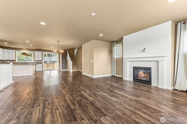 unfurnished living room featuring a fireplace, dark wood finished floors, baseboards, an inviting chandelier, and recessed lighting