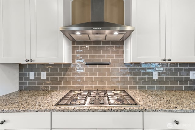 kitchen with wall chimney range hood, light stone counters, stainless steel gas stovetop, and white cabinetry
