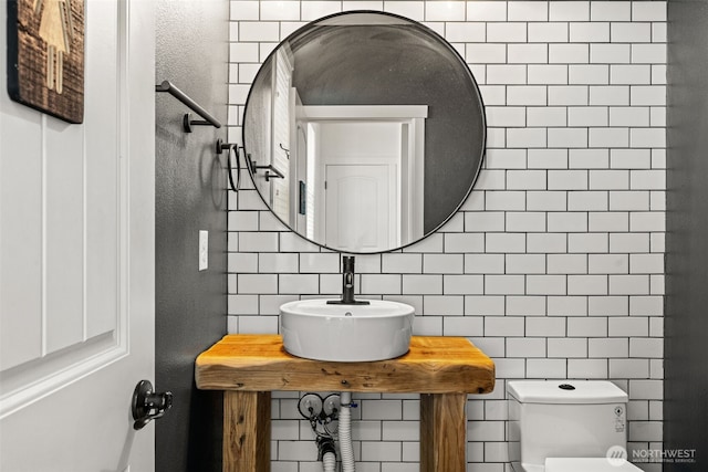 half bath featuring toilet, tile walls, a sink, and tasteful backsplash