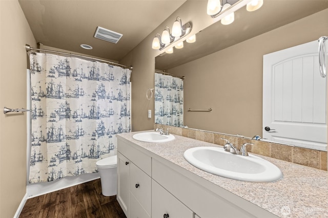bathroom with a sink, toilet, wood finished floors, and visible vents