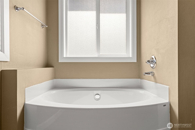 bathroom featuring a textured wall and a bath