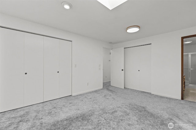 unfurnished bedroom featuring two closets, baseboards, carpet, and ensuite bath