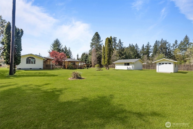 view of yard featuring a garage, fence, and an outbuilding