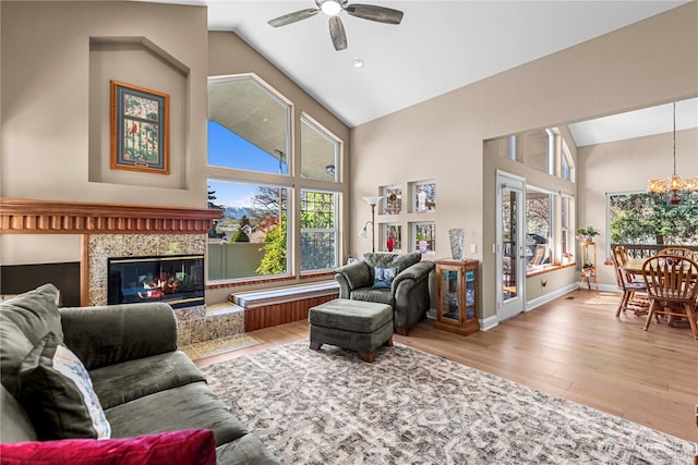 living area with a fireplace, wood finished floors, high vaulted ceiling, and ceiling fan with notable chandelier