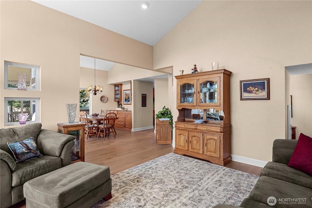 living room featuring baseboards, wood finished floors, high vaulted ceiling, and a notable chandelier
