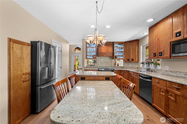 kitchen with brown cabinets, a sink, a center island, appliances with stainless steel finishes, and a notable chandelier