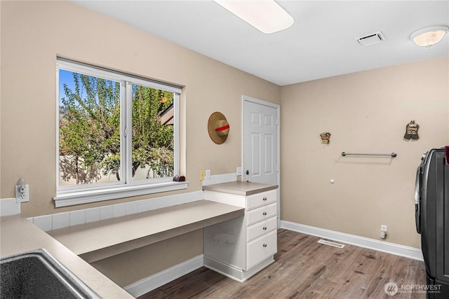office with light wood finished floors, baseboards, visible vents, and built in study area