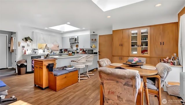kitchen with open shelves, stainless steel microwave, light wood-type flooring, a skylight, and a peninsula