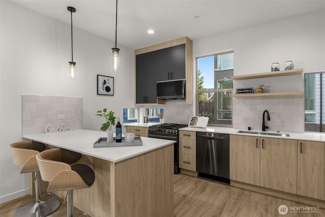 kitchen featuring stainless steel appliances, a sink, light brown cabinets, a kitchen bar, and light wood-type flooring