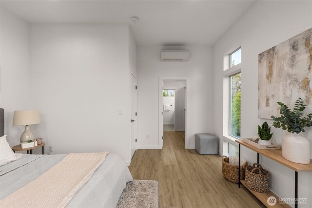 bedroom featuring a wall mounted air conditioner, light wood-style flooring, and baseboards