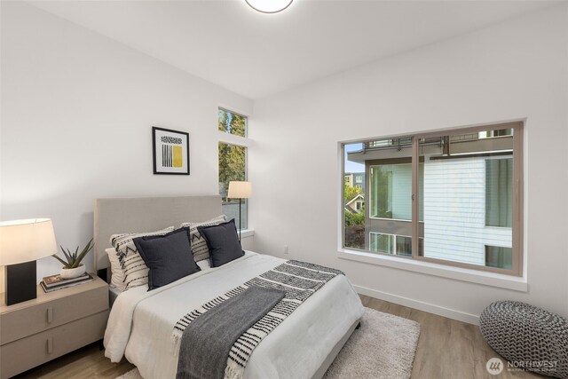 bedroom with multiple windows, wood finished floors, and baseboards