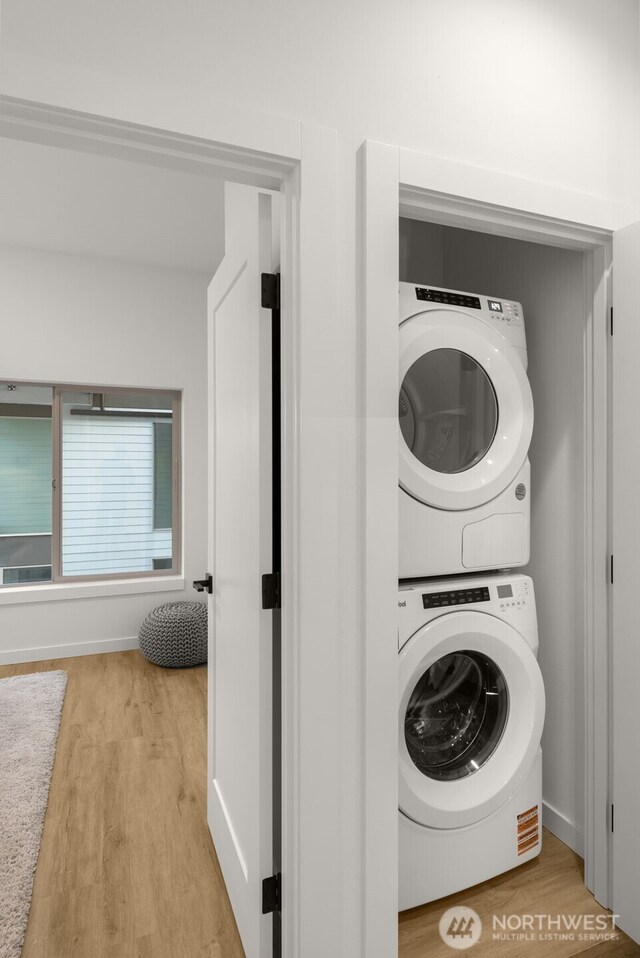 washroom with estacked washer and dryer, light wood-style floors, and baseboards