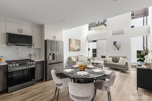 dining room featuring light wood finished floors, a wall mounted AC, and a towering ceiling