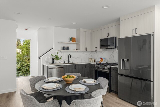 kitchen featuring appliances with stainless steel finishes, a sink, open shelves, backsplash, and light wood-type flooring
