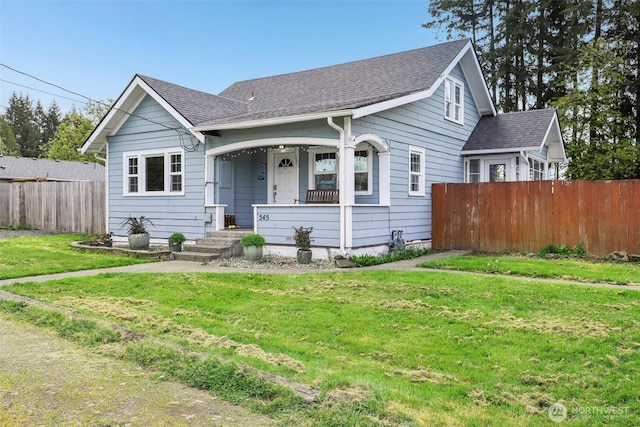 bungalow-style home with covered porch, fence, a shingled roof, and a front yard