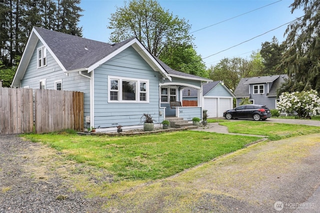 view of front of home featuring roof with shingles, fence, a detached garage, and a front lawn