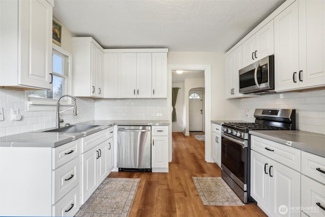 kitchen featuring appliances with stainless steel finishes, a sink, white cabinetry, wood finished floors, and tasteful backsplash