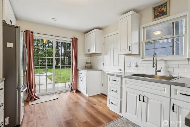 kitchen with decorative backsplash, light wood-type flooring, a sink, white cabinets, and freestanding refrigerator
