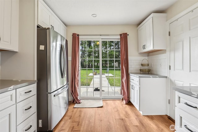 kitchen featuring light wood-style floors, freestanding refrigerator, decorative backsplash, and white cabinets