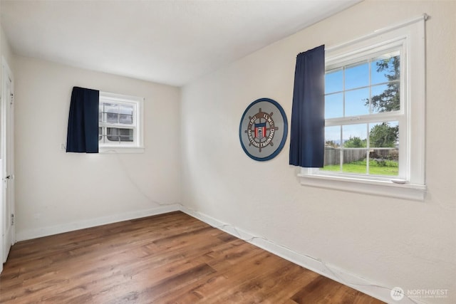 unfurnished room with baseboards, wood finished floors, and a wealth of natural light