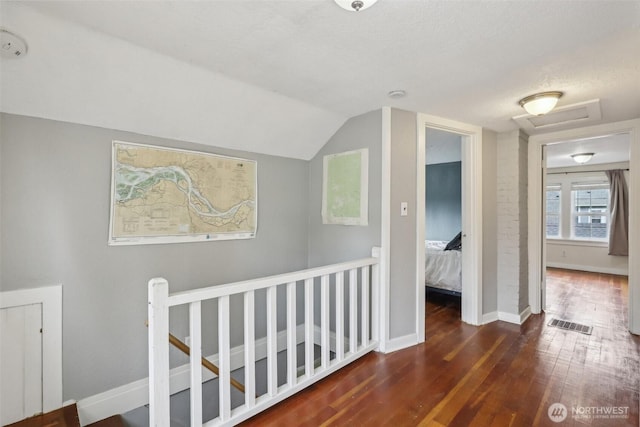 corridor featuring attic access, visible vents, an upstairs landing, wood-type flooring, and lofted ceiling