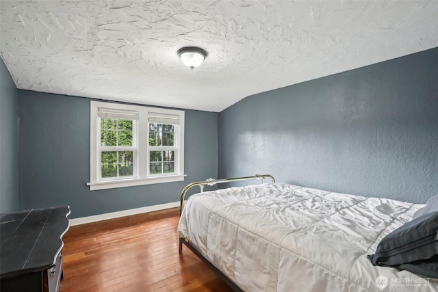 bedroom featuring wood-type flooring, baseboards, and a textured wall
