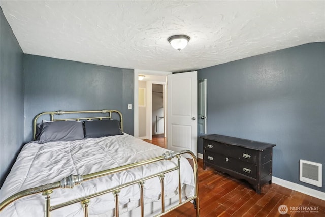 bedroom featuring baseboards, a textured ceiling, wood finished floors, and visible vents