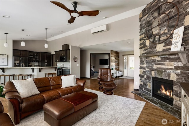 living room with lofted ceiling, wood finished floors, a ceiling fan, a fireplace, and a wall mounted AC