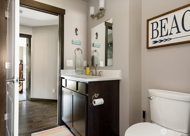half bathroom with toilet, vanity, wood finished floors, and baseboards