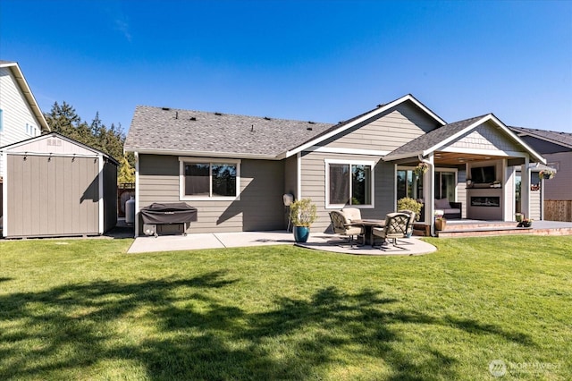 back of house with a shingled roof, a yard, a shed, an outdoor structure, and a patio