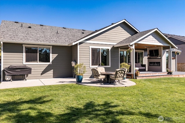 rear view of house featuring a shingled roof, a yard, and a patio