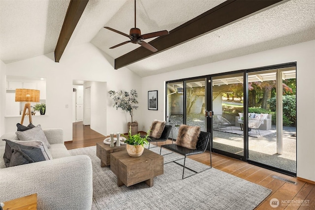 living room with visible vents, wood finished floors, vaulted ceiling with beams, a textured ceiling, and a ceiling fan