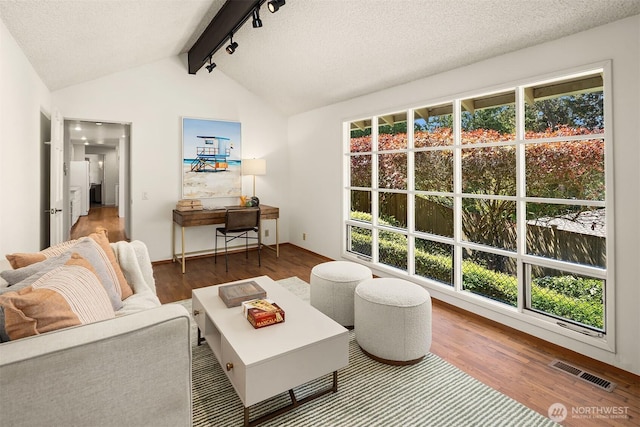 living room with a textured ceiling, visible vents, rail lighting, wood finished floors, and vaulted ceiling with beams