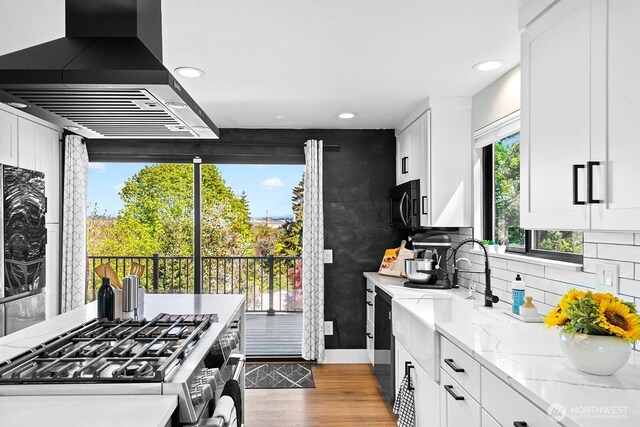 kitchen with light stone counters, wood finished floors, a sink, island range hood, and stainless steel appliances