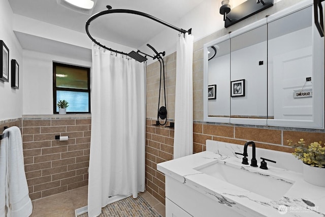full bathroom featuring tile patterned floors, vanity, tile walls, a wainscoted wall, and tiled shower
