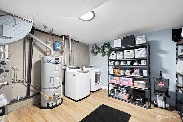 clothes washing area featuring washing machine and dryer, wood finished floors, strapped water heater, and laundry area