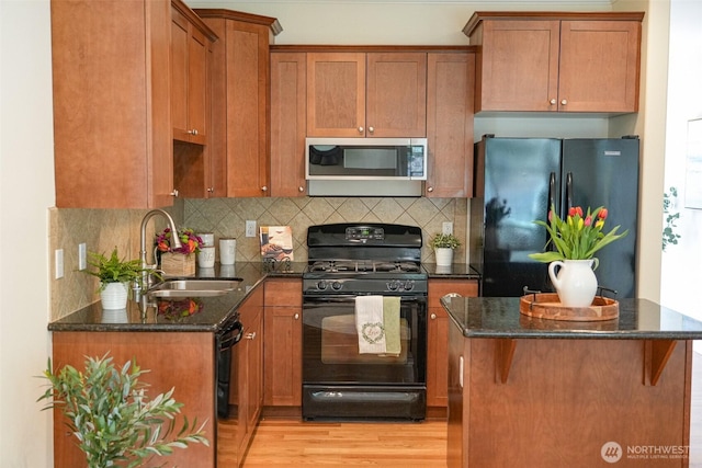 kitchen with brown cabinetry, a sink, dark stone countertops, backsplash, and black appliances