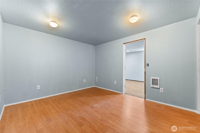unfurnished room with wood finished floors, a textured ceiling, and baseboards