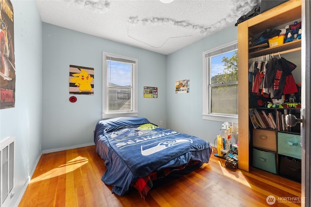 bedroom featuring a closet, wood finished floors, a textured ceiling, and multiple windows