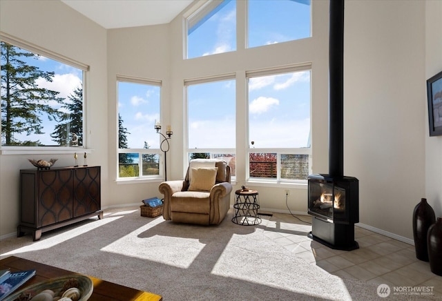 interior space with light tile patterned floors, baseboards, a high ceiling, and a wood stove